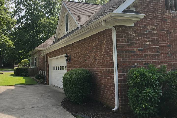 Red brick Georgia home with white gutters and a downspout beside the garage under mature shade trees