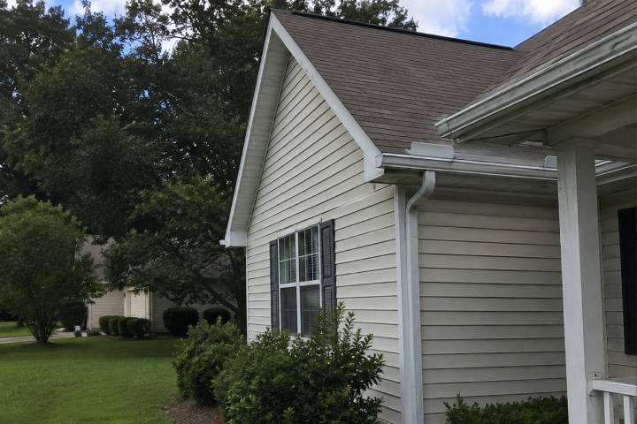 Coastal style Georgia cottage with white gutters shaded by a large hardwood canopy ahead of hurricane season