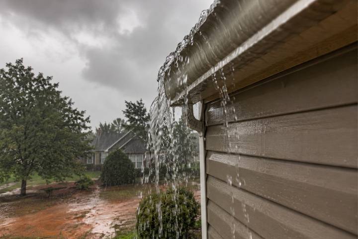 where-should-your-downspouts-drain-in-georgias-red-clay-yards-1 Rain overshooting a clogged gutter at the corner of a Georgia home and pooling on the red clay yard during a storm