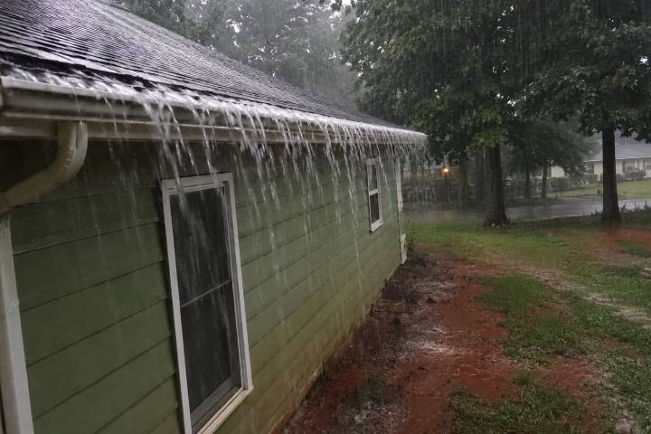 Stormwater sheeting over a blocked gutter on a green Georgia ranch house with eroded red clay ground below